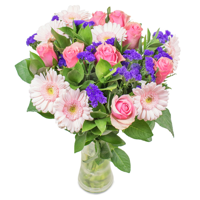 This sophisticated floral display brings together expertly chosen blooms by the skilled team at Florist Cubitt Town. Approximately seven to nine classic pink roses, some tightly furled and others just beginning to open, are the visual heart of the composition. Five to seven large, pale pink gerbera daisies with softly radiating petals and light, nearly white centers add gentle contrast. Scattered throughout are clusters of vivid purple statice, functioning as elegant fillers that provide texture and a dash of deeper colour, all resting amid a lush mantle of deep green leaves. Set in a transparent glass vase-its water and stems visible-the arrangement exudes freshness, conjuring images of a bouquet picked from the riverside gardens near Island Gardens DLR. Designed for delivering joy on occasions from birthdays to anniversaries and Mother's Day throughout Cubitt Town, this bouquet is equally at home as an uplifting feature in Docklands offices or apartments. Each floral choice reflects an expert's attention to detail and a nod to Isle of Dogs' bright, community spirit.